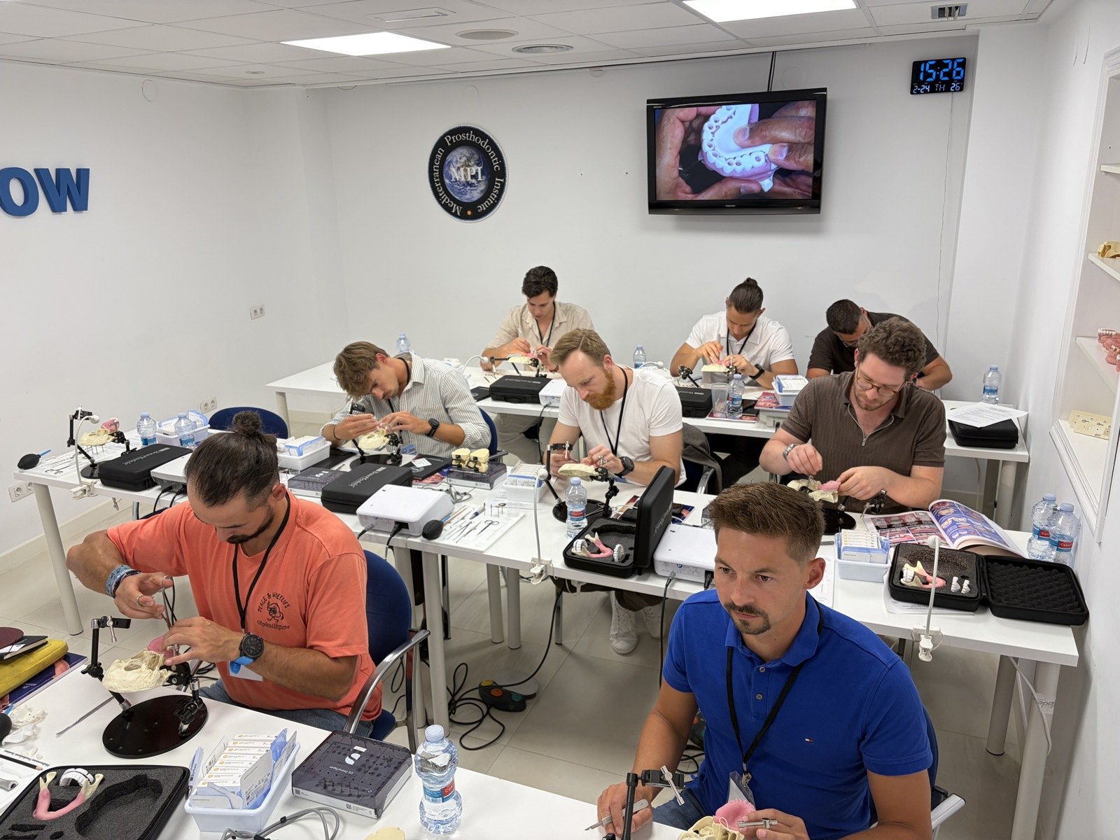Účastníci workshopu pracujú s dentálnymi modelmi pri samostatných stoloch.